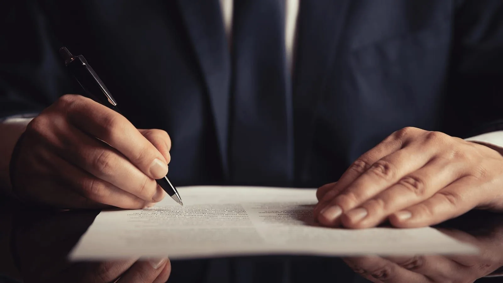 A person in a suit signing a document at a desk