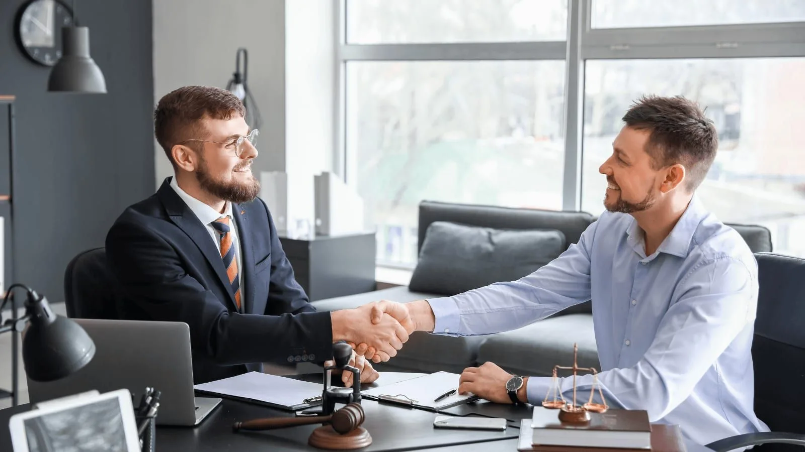 Two people shaking hands across a desk in an office