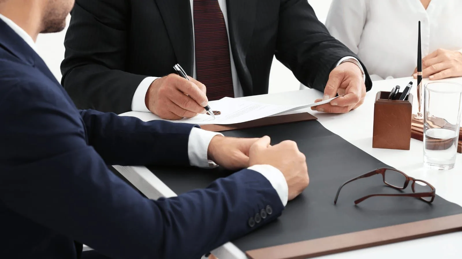 Several people seated at a table as one of them signs an agreement